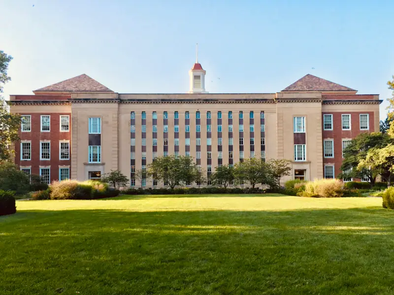 Large academic building with a formal stone and brick facade, set behind a lawn